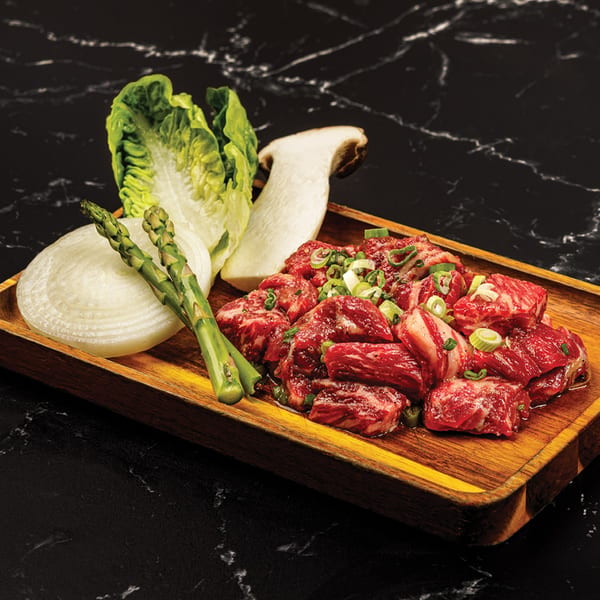 Antoya Korean BBQ's marinated beef cubes, lettuce, onion, asparagus, and mushroom on a wooden tray.