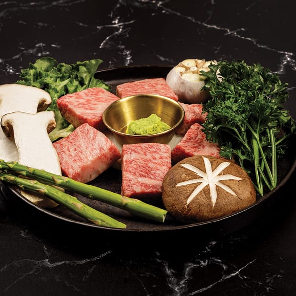 Antoya Korean BBQ raw beef cubes, mushrooms, asparagus, garlic, and herbs on a dark platter.