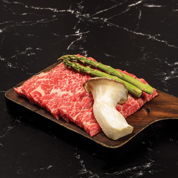 Antoya Korean BBQ's raw marbled beef slices, asparagus, and king oyster mushroom on a wooden board.