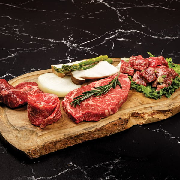 Assortment of raw beef cuts, onions, asparagus, and mushrooms on a wooden board.