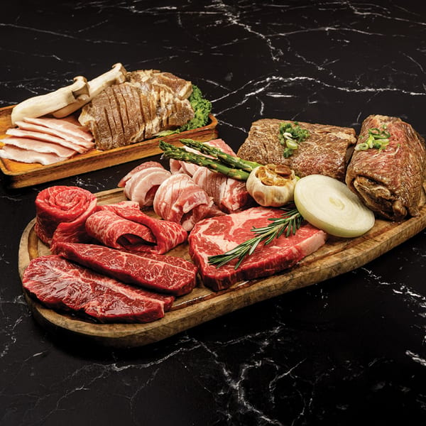 Assortment of raw Korean BBQ meats, including beef, pork belly, mushrooms, and asparagus on wooden boards.