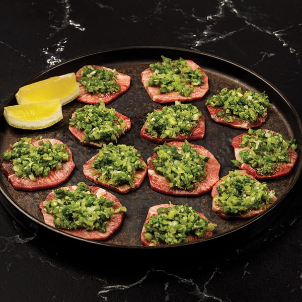 Antoya Korean BBQ beef tongue slices topped with chopped green onions and two lemon wedges.